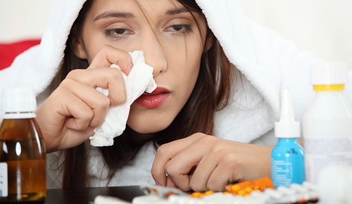 Woman sick in bed with a bunch of tissues and medicine